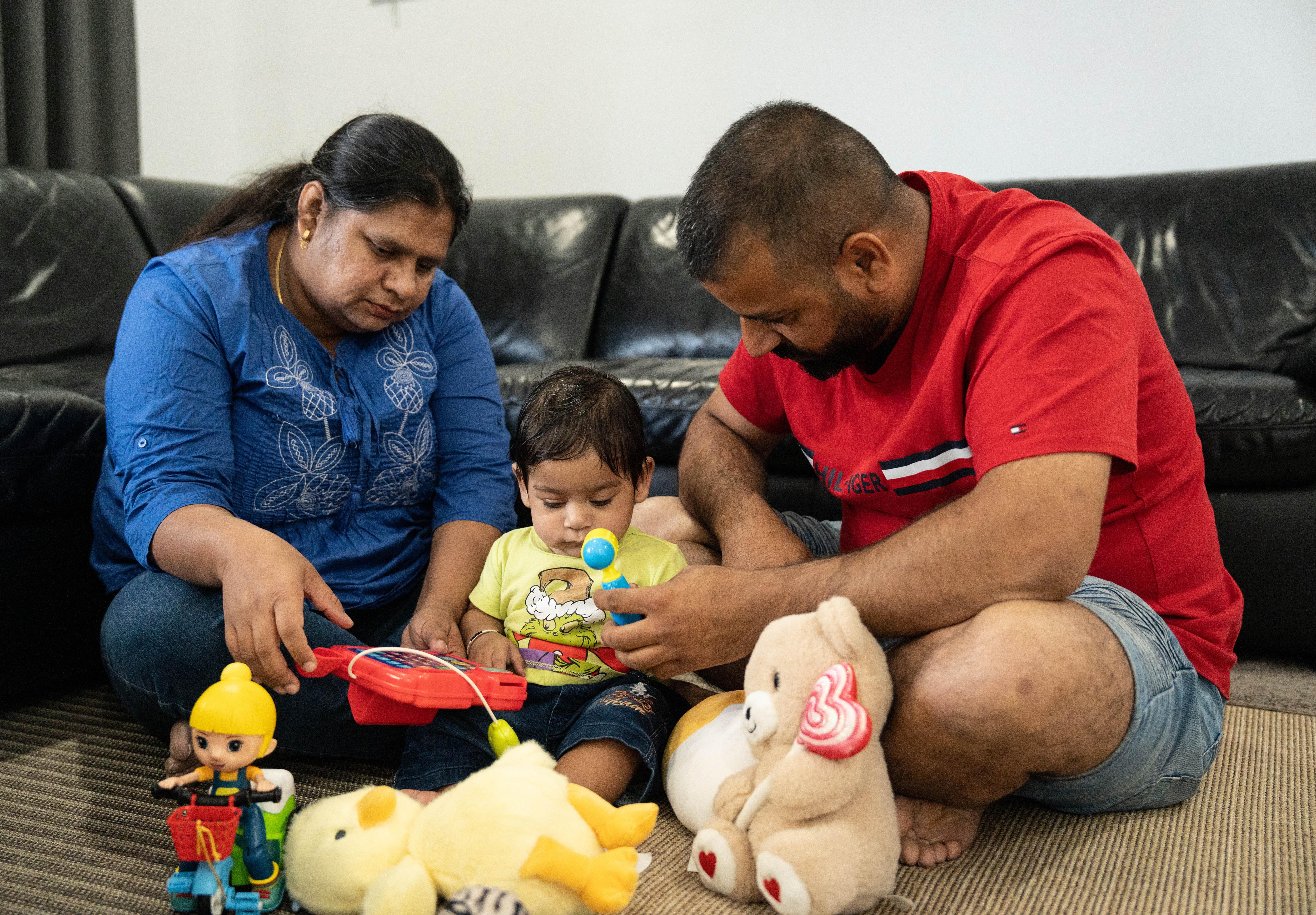 A woman and a man sitting on a carpeted floor with a young boy in front of a black sofa