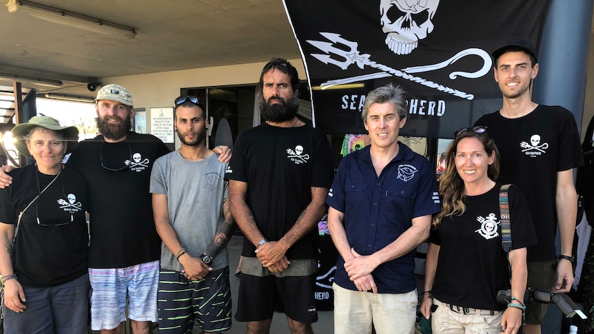 Members of conservation group Sea Shepherd standing in front of their iconic flag at Mackay Harbour.