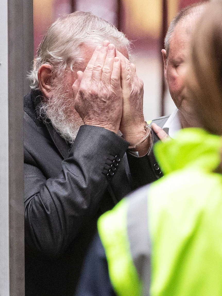 A man with white hair and a white beard covers his face.