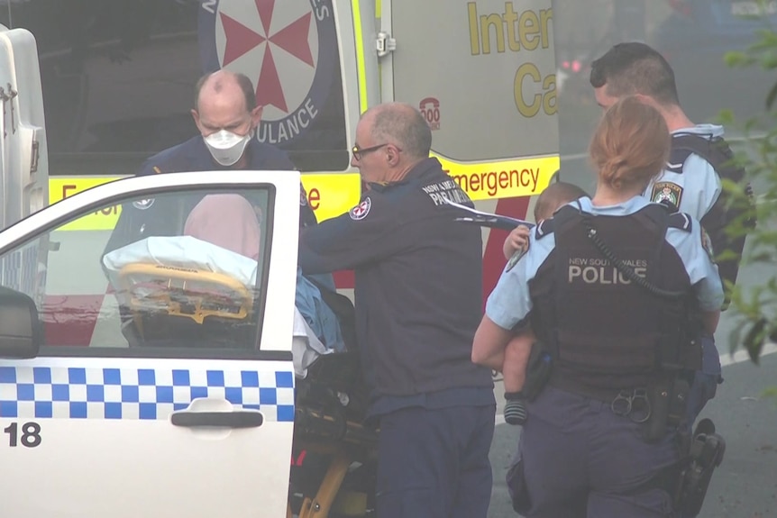 Paramedics treat a woman on a stretcher while the police stand next to her
