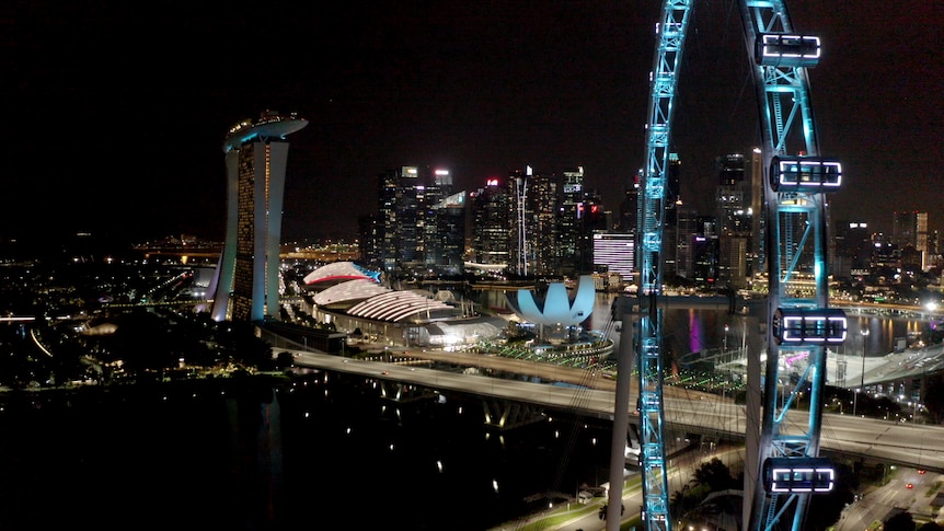 An aerial shot of several buildings and an observation wheel lit up at night in Singapore.