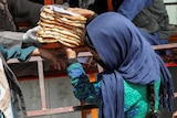 A woman wearing a headscarf receives a stack of flat bread from a man who is wearing a face mask as he hands out rations.