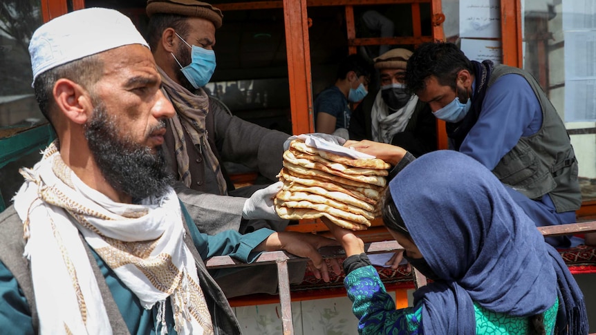 A woman wearing a headscarf receives a stack of flat bread from a man who is wearing a face mask as he hands out rations.