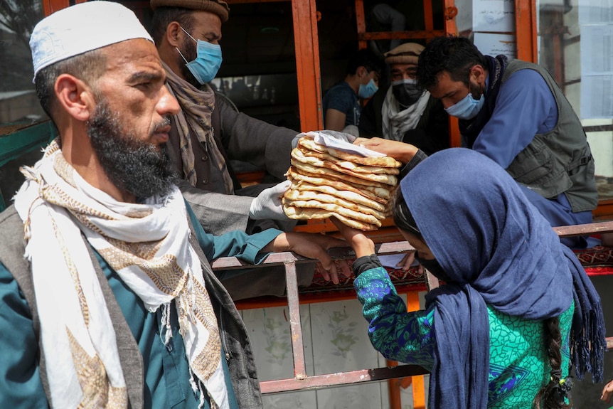 A woman wearing a headscarf receives a stack of flat bread from a man who is wearing a face mask as he hands out rations.