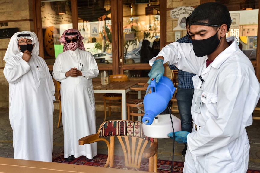 Worker wearing overalls, gloves and mask sanitises a table at a cafe in Riyadh.
