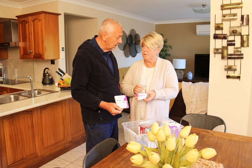 Tanya Battel, stands with her husband George in their kitchen in their home in Brisbane, looking at her medications.
