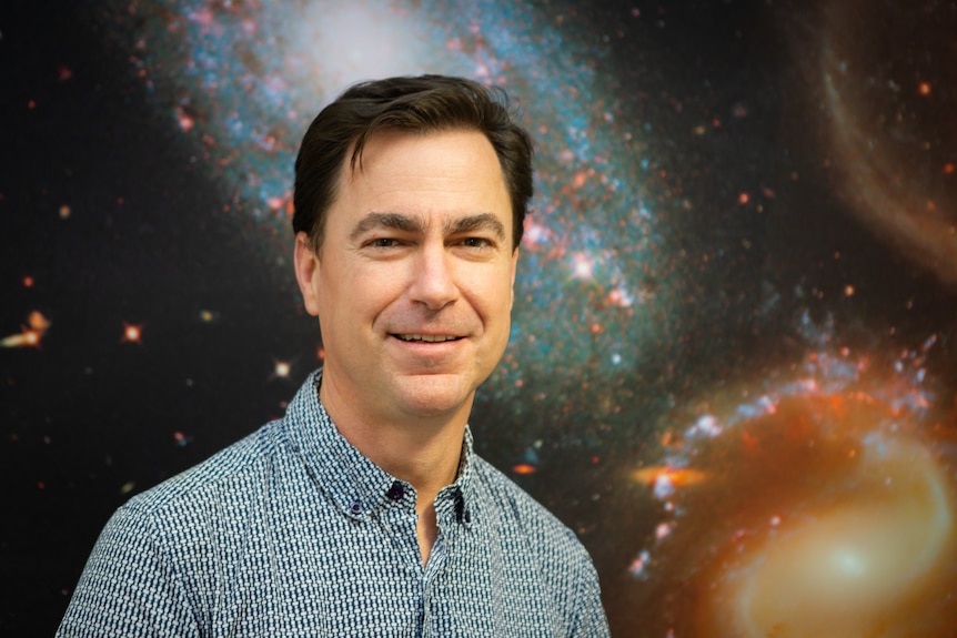 a man standing in front of a galaxy background smiling