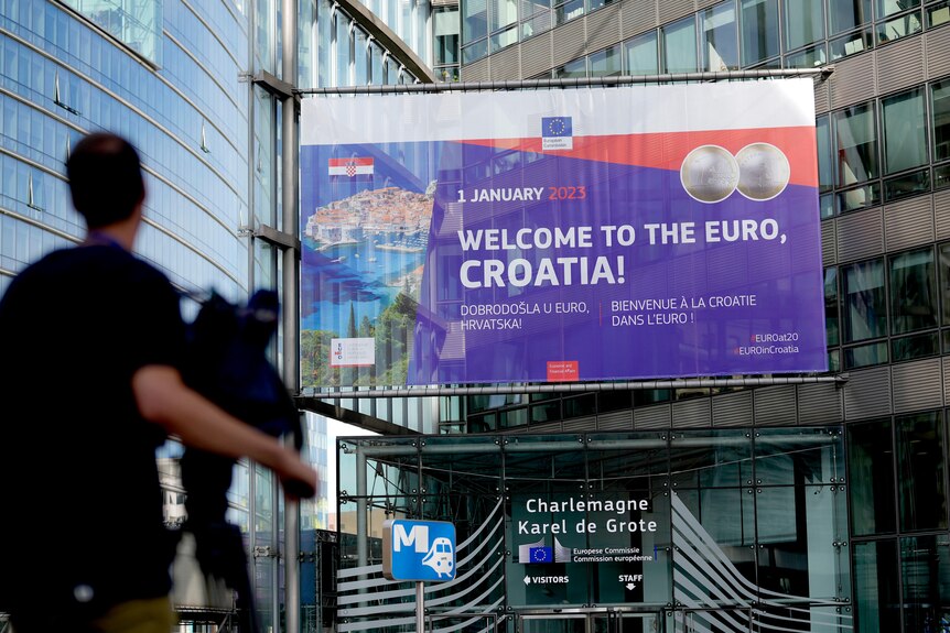 A journalist films a banner welcoming Croatia to the euro in front of EU headquarters in Brussels.