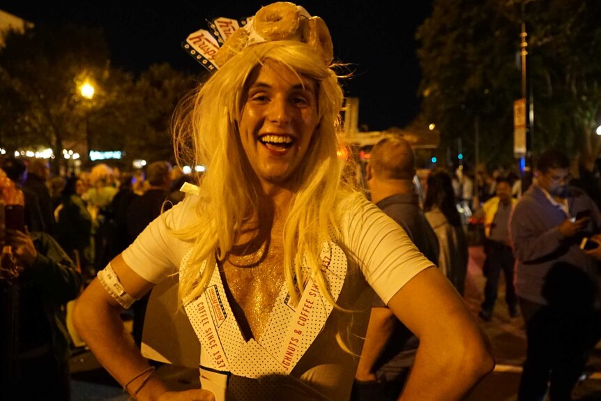 Drag queen posing on a street at night-time, surrounded by people