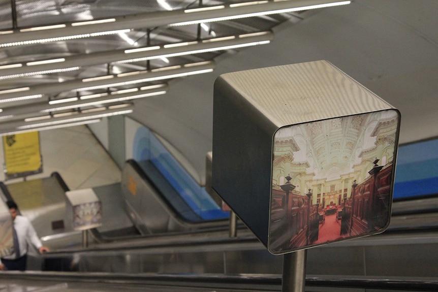A metal box with an image of an old theatre is one of many images on the steep Parliament Station escalators.