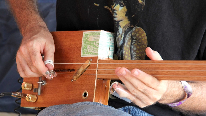 A stall owner plays one of his cigar box guitars.