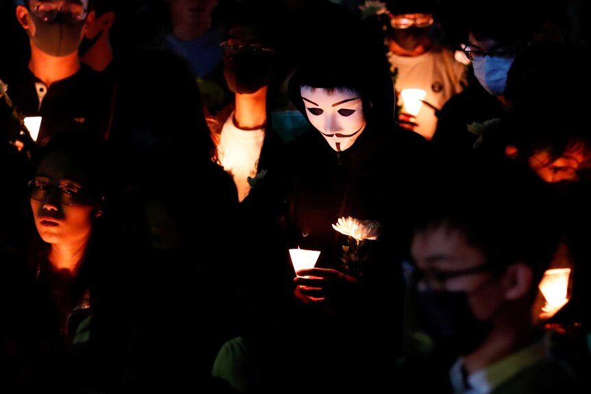 Fellow students, one in a Guy Fawkes mask light candles for Chow Tsz-lok, who died on Friday.