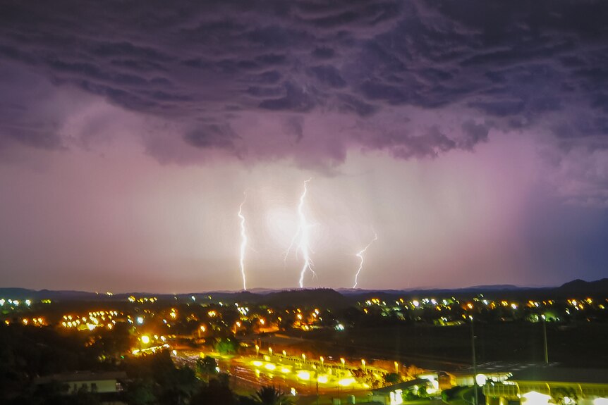 Lightning and storm clouds over a town, lit up at night.