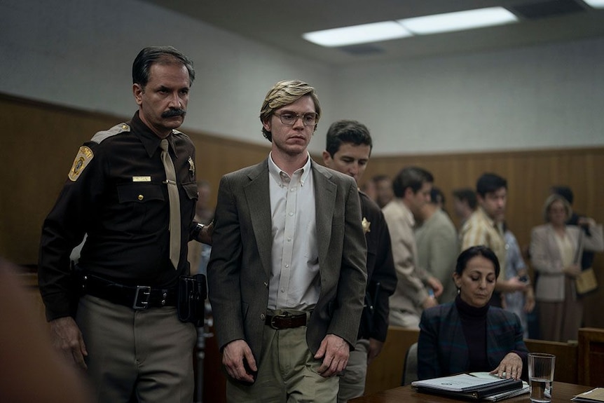 A scene from the Netflix series of Jeffrey Dahmer inside a courtroom being escorted by two policemen