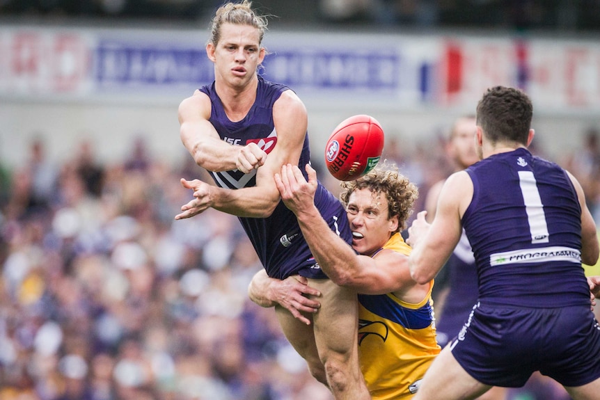 Nat Fyfe handballs a red football to a teammate while being tackled by Matt Priddis during an AFL match.