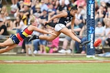 Carlton AFLW player stretches mid-air to boot the ball for a goal, beating a despairing defender.