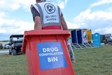 A man drags a wheelie bin with the words "drugs confiscation bin" on it