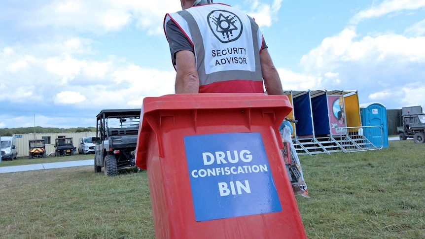 A man drags a wheelie bin with the words "drugs confiscation bin" on it