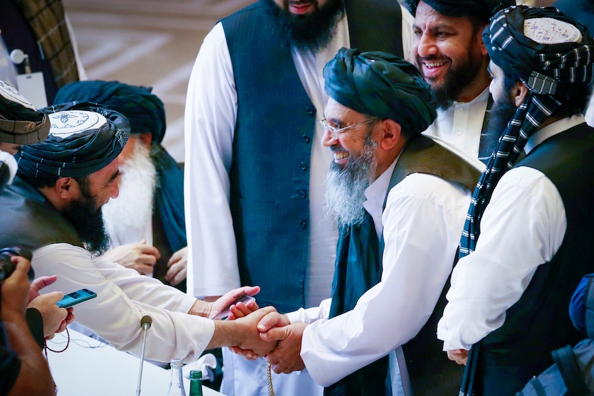 A group of men with beards, dressing in pakol hats, grinning and shaking hands 