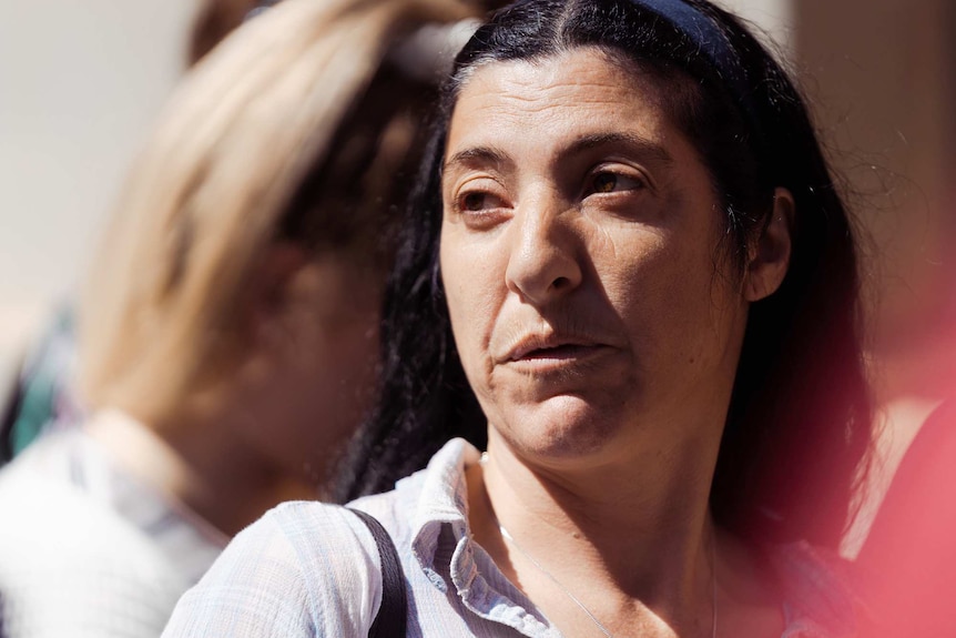 A tight head shot of a middle aged woman with dark hair outdoors.