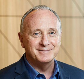 A smiling portrait of a middle aged man wearing a navy shirt and jacket.