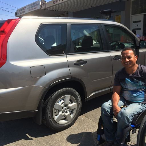 Joel Fernandes sits in a wheelchair, outside his car.