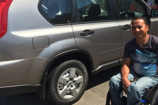 Joel Fernandes sits in a wheelchair, outside his car.