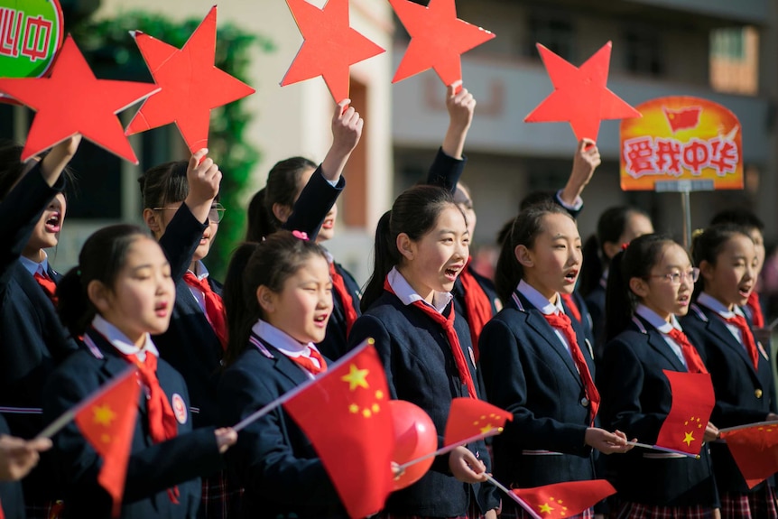 Young female students in uniforms hold stars and Chinese flags while singing