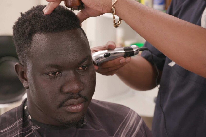 John Kuot sits in a barber's chair getting his hair cut.
