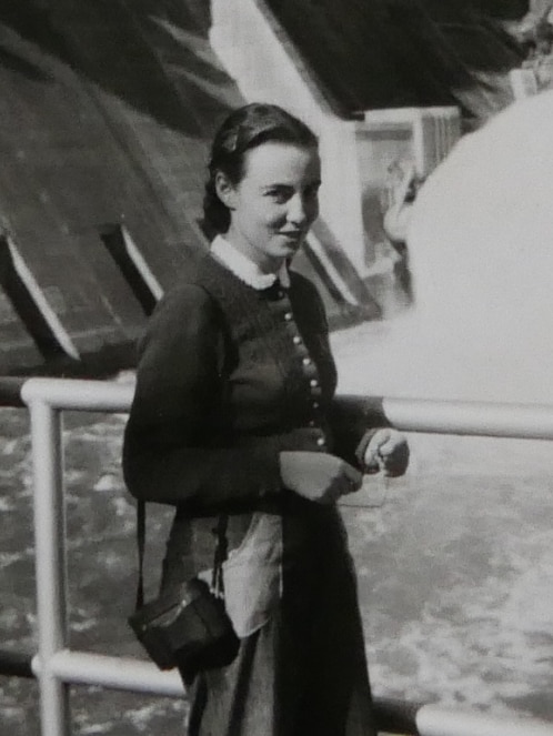 A young woman from the 1950s stands in front of a flowing dam.