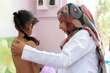 A doctor in a hijab treats a child in a hospital room.
