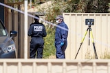 Forensics officers wearing masks and suits stand next to a car 