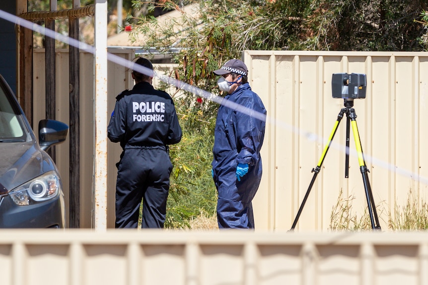 Forensics officers wearing masks and suits stand next to a car 