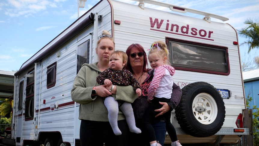 A mother, her adult daughter and two small kids stand in front of a caravan.
