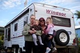A mother, her adult daughter and two small kids stand in front of a caravan.