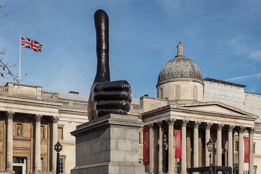 A large bronze sculpture of a thumbs up sits on a plinth in Trafalgar Square, London, in front of the National Gallery.
