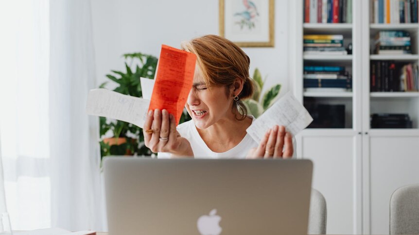 A woman is holding bills in her hands in front of her laptop and crying