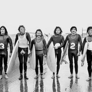 Un grupo de hombres en trajes de neopreno con tablas de surf, una fotografía en blanco y negro