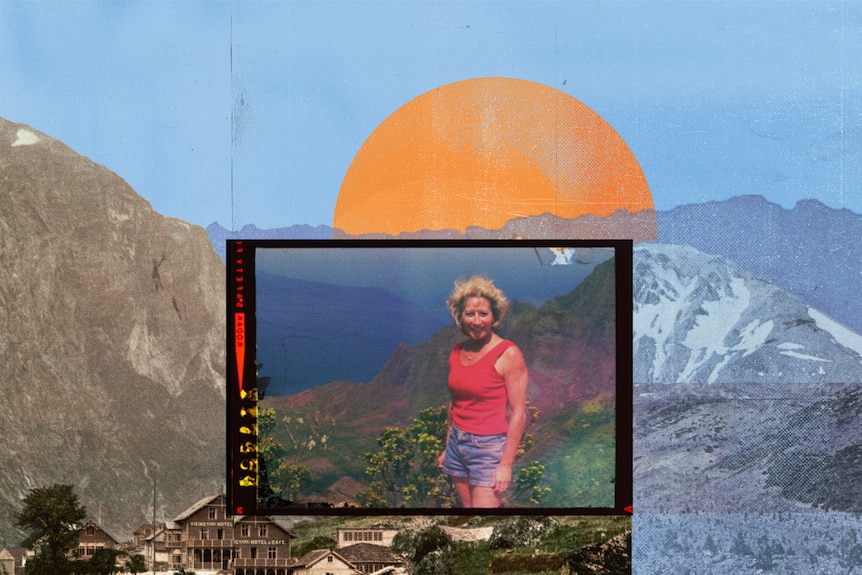 A woman in tank to and shorts stands smiling in sun on mountain side near water.