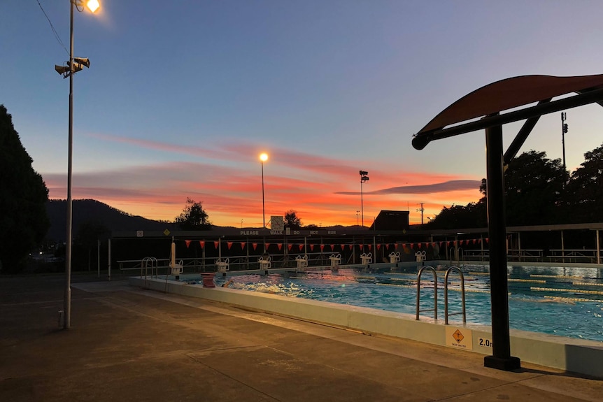 An outdoor swimming pool at dusk or dawn, with pink clouds in the sky