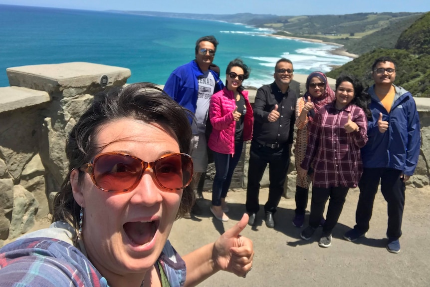 A woman takes a selfie along great ocean road with tourists in huddle behind her