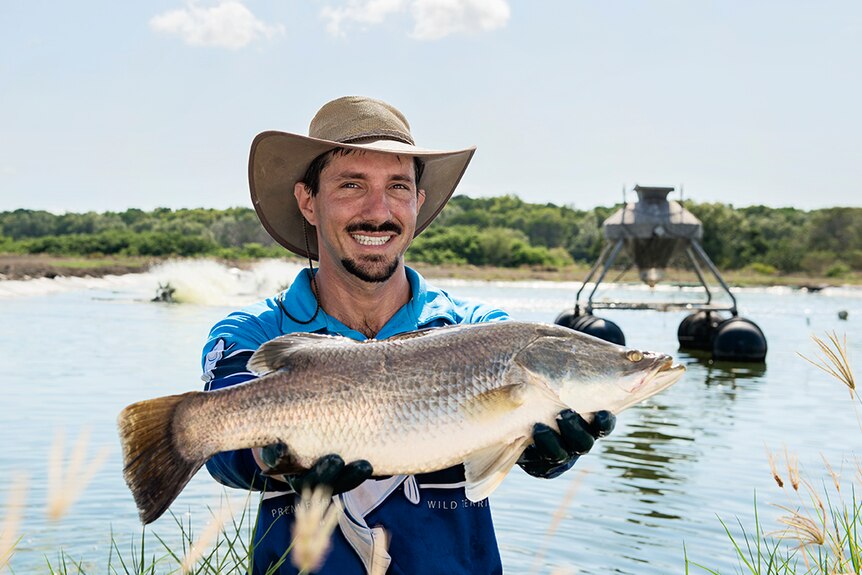 man smiling holding a barramundi on a fish farm