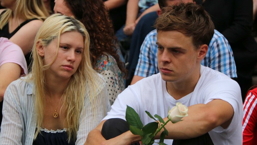 A woman sits beside a man holding a flower at the vigil in front of Parliament House.