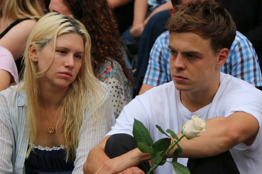 A woman sits beside a man holding a flower at the vigil in front of Parliament House.