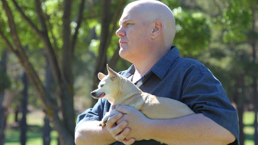 A man holding a dog looks off into the distance.