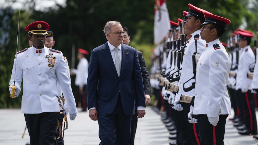 Anthony Albanese walks past an honour guard of Singapore armed forces personnel in white dress uniforms.