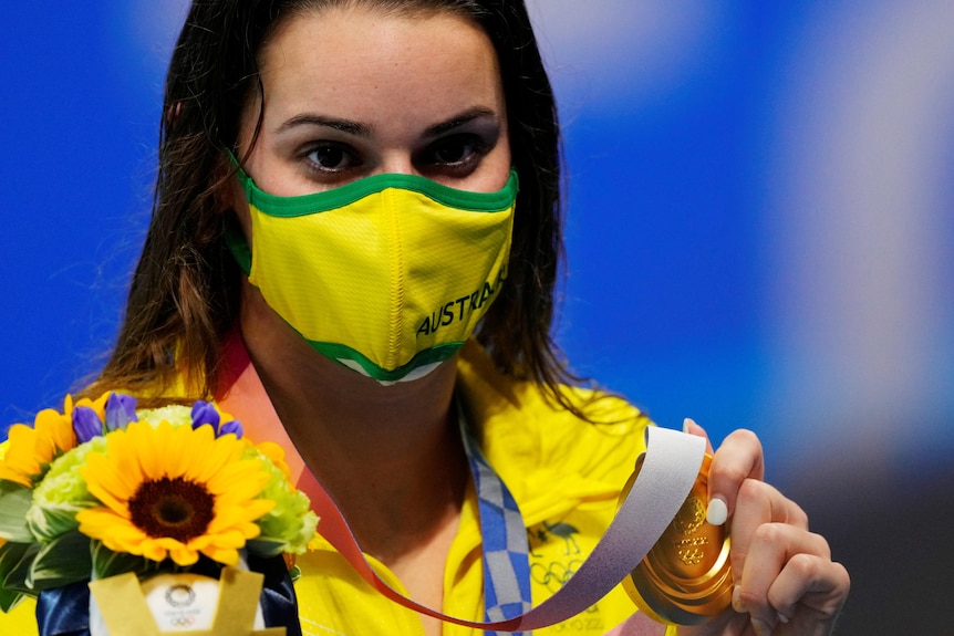 Kaylee McKeown poses with her gold medal for swimming while wearing a green and gold face mask.