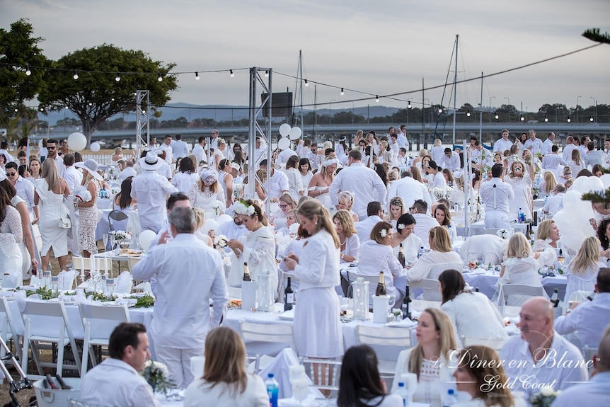 Un grand rassemblement de personnes vêtues de blanc lors d'un dîner en plein air
