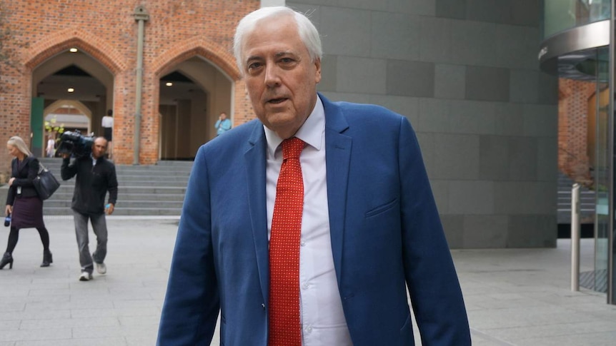 Clive Palmer walks away from the Perth Supreme Court, a tv crew is walking in the background.