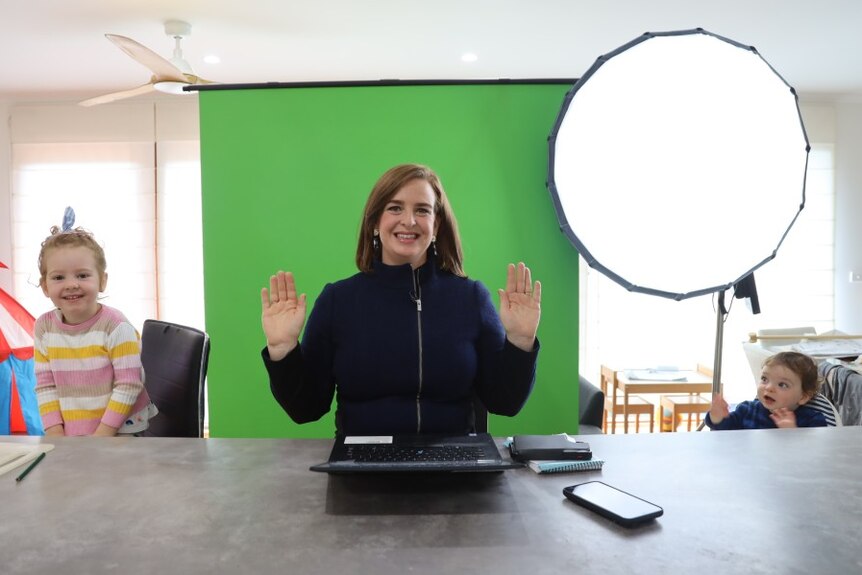 Henderson standing in front of green screen with two children sitting next to her.